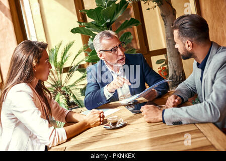 Professional team. Positive nice smart colleagues sitting together in the cafe and discussing their project while working in team Stock Photo