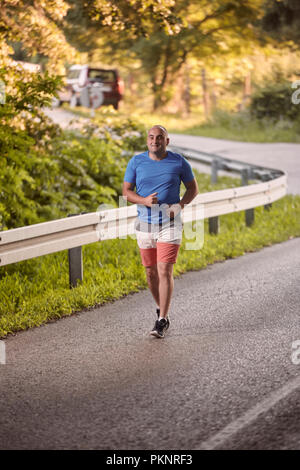one young overweight man, outdoors nature, running on asphalt road. full length shot, trees, beautiful scenery, vegetation. National park Fruska Gora, Stock Photo