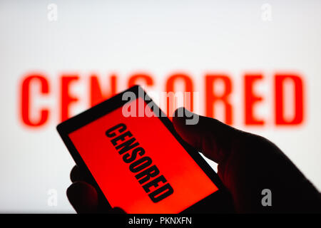 A smartphone in hand displaying the "censored" text. Same text in red blurred on white background. The concept of censorship on popular social network Stock Photo