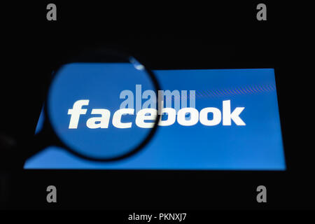 MOSCOW, RUSSIA - September 14, 2018: Smartphone lying on a table in the dark, displaying logo of the Facebook. The magnifying glass above touch screen Stock Photo