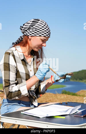 Girl archaeologist carefully cleans the find - part of the spine of a medieval mammal. The pleasure of working in a field expedition Stock Photo