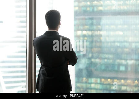 Successful thoughtful businessman looking through the window at  Stock Photo