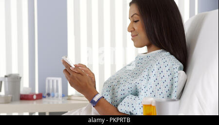 Black woman using smart phone in hospital bed Stock Photo