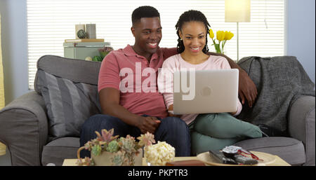 Happy black couple on couch browsing internet with laptop computer Stock Photo