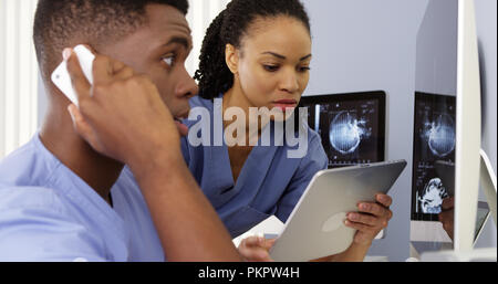 Two African American doctors using tablet and phone to work together Stock Photo
