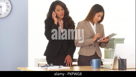 Two mixed race colleagues talking on smartphone and using tablet Stock Photo