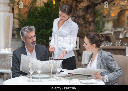 waitress offering tasty dishes to smiling guests couple Stock Photo
