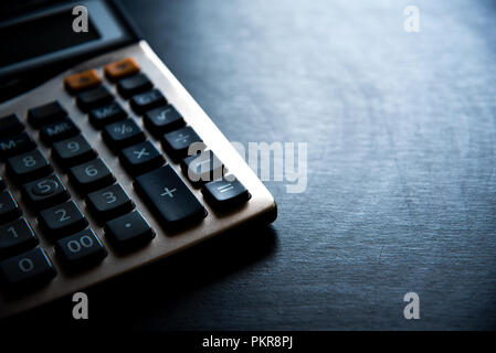 calculator on wooden table and dark background, part of calculator in blue tone Stock Photo