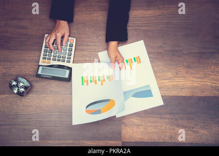 hand holding graph sheet and pressing calculator on wooden table, business man holding hand on wooden table and holding paper of graph data Stock Photo