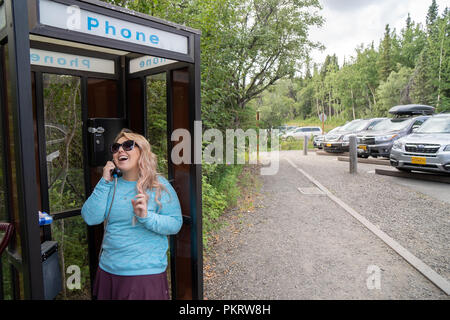 Blonde female talks on a landline telephone in a retro phone booth. Concept for retro technology, outdated technology Stock Photo