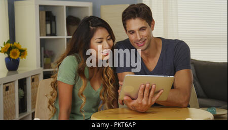 Happy mixed race couple talking on tablet Stock Photo