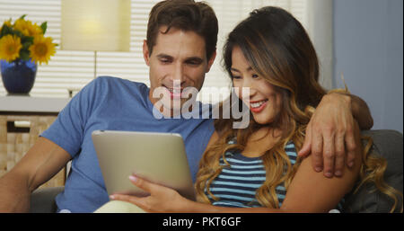 Happy interracial couple using tablet together on couch Stock Photo