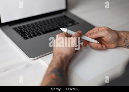 Male artist works in a laptop and holds a pen of a graphic tablet Stock Photo