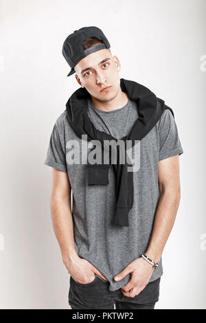Stylish young man with a baseball cap in a gray t-shirt posing in the studio. Stock Photo