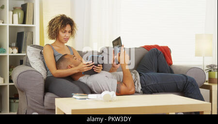 Black couple using their tablets on couch Stock Photo