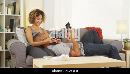 Black couple using their tablets on couch Stock Photo