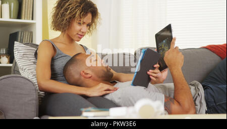 African couple using tablets on couch Stock Photo