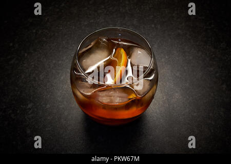 An isolated glass of bright, amber / brown alcoholic drink with ice and orange slices against a black background Stock Photo