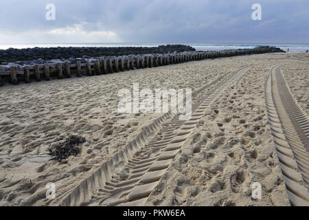 Big tire tracks on an empty beach in the Landes in France on a very stormy day with an old stones and wood pier Stock Photo