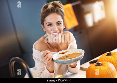 Adult woman eating pumpkin soup in the kitchen Stock Photo