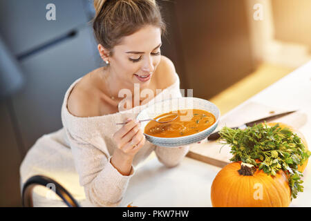 Adult woman eating pumpkin soup in the kitchen Stock Photo