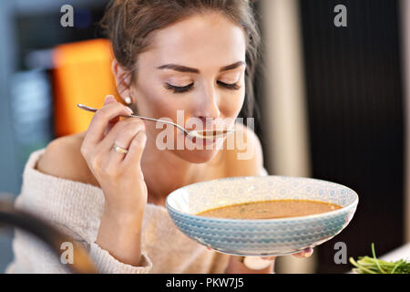 Adult woman eating pumpkin soup in the kitchen Stock Photo