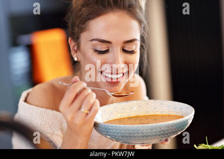 Adult woman eating pumpkin soup in the kitchen Stock Photo