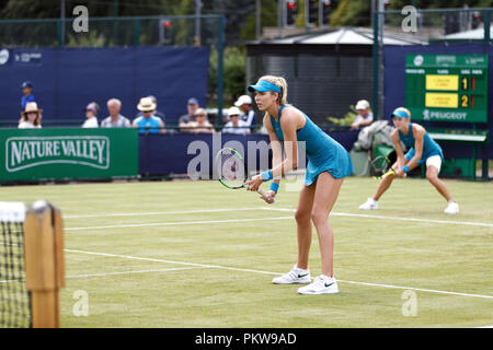 British tennis players Katie Boulter (foreground) and Katie Swan (background) await their opponent's serve during a women's doubles match at a professional grass court tournament in the United Kingdom. Boulter and Swan played together in matching outfits.