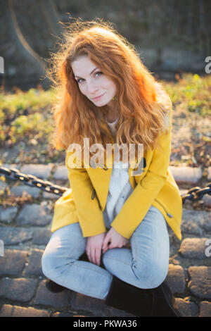Red hair beautiful woman wearing yellow coat walking outdoors. Autumn time, city on background Stock Photo