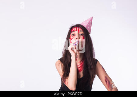 Halloween and carnival concept - young woman with blood on face celebrate holidays with whistle Stock Photo