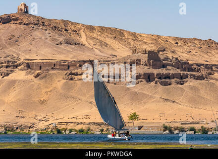 Qubbet el Hawa domed hilltop tomb and ancient tombs in desert cliff, West bank, with felucca sailing boat on River Nile, Aswan, Egypt, Africa Stock Photo