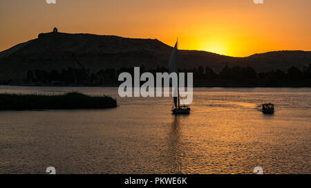 Silhouettes of tradional felucca sailing boats at sunset in River Nile with hilltop monument Qubbet el Hawa, Aswan, Egypt, Africa Stock Photo