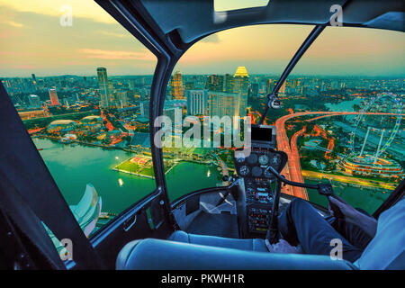 Scenic helicopter flight above Singapore twilight panorama at dawn. Night urban aerial scene from the cockpit interior with Singapore cityscape with ferris wheel at sunset. Stock Photo
