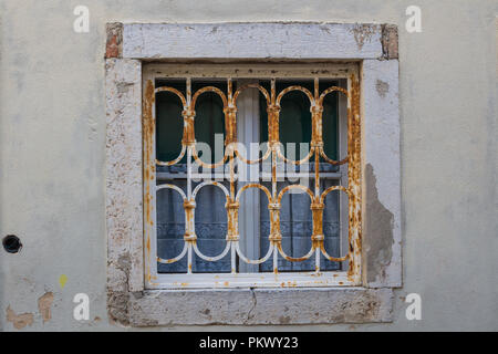 Small window of an old historic house with a white frame, rusted grating and traditional white curtains. City centre of city Krk, island Krk, Croatia. Stock Photo