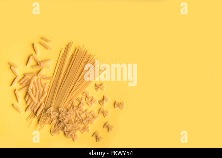 Assorted various uncooked raw pasta on yellow background, copy space. Italian pasta: penne, farfalle, spaghetti. Stock Photo