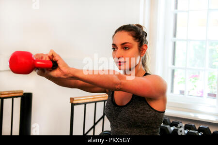 Female fitness exercise with kettle bell swings for legs and shoulders. Attractive young woman doing kettle bell swings in a cross-training gym. Sport Stock Photo
