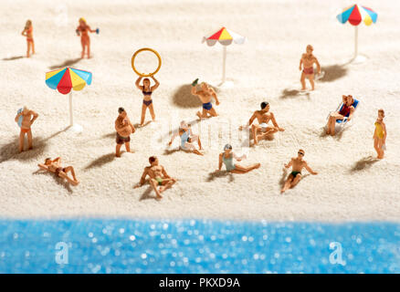 Lots of little miniature people sunbathing on a sandy beach with sparkling blue ocean conceptual of summer vacations and a healthy outdoor lifestyle Stock Photo