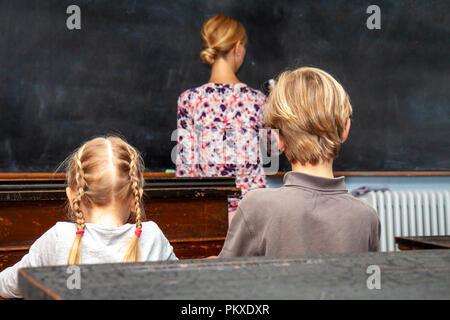 Concept of public primary school education with young boy and girl listening to the female teacher. Stock Photo