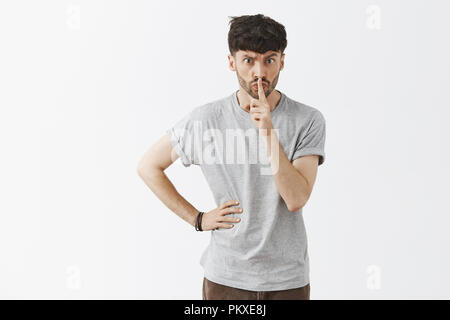I order you keep quiet. Serious displeased and strict aduly male teacher with stylish hairstyle and beard saying shh while showing shush gesture with index finger over mouth demanding silence Stock Photo