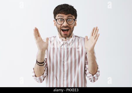 Waist-up shot of enthusiastic excited attractive guy in glasses clapping hands after having great idea or liking lecture smiling broadly with excitement and amazement feeling happy over gray wall Stock Photo