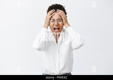 Hold on, I need break. Tired distressed upset african-american female in glasses, closing eyes, yelling from painful feeling, holding hand on head, losing important deal, devastated and displeased Stock Photo