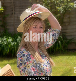 Woman wearing a floral summer dress putting on a straw hat Stock Photo