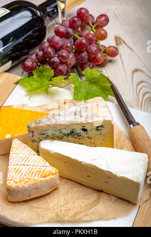 Tasting plate with four France cheeses, cream brie, marcaire, saint paulin and blue auvergne cheese, served with fresh ripe grapes close up Stock Photo