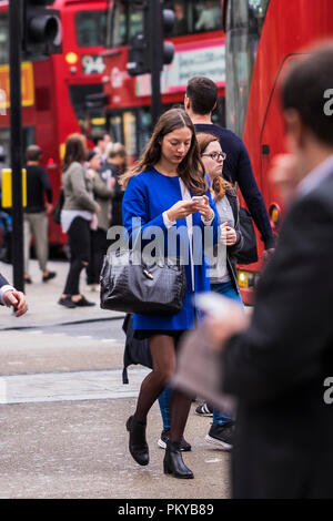 Woman using smartphone crossing the road, Oxford Street, London, England, U.K. Stock Photo