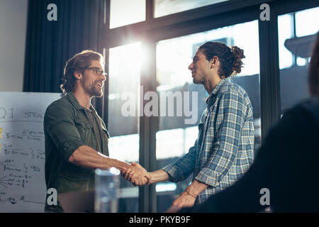 Young businessman shaking hands with male colleague after meeting in boardroom. Business handshake after successful meeting. Stock Photo