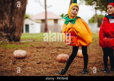 Two little girls in pumpkin costume holding halloween buckets. Identical twin sisters ready for treat or tricking outdoors. Stock Photo