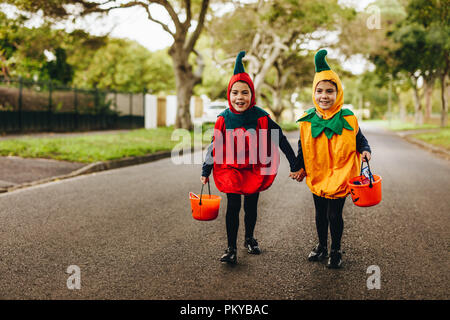 Two little girls in halloween costume trick or treating on the road. Two identical twin sisters in halloween costume walking outdoors with halloween b Stock Photo