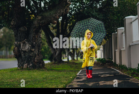 Portrait of beautiful young girl walking outdoors on a rainy day wearing waterproof clothes and rubber boots. Girl wearing raincoat walking with umbre Stock Photo
