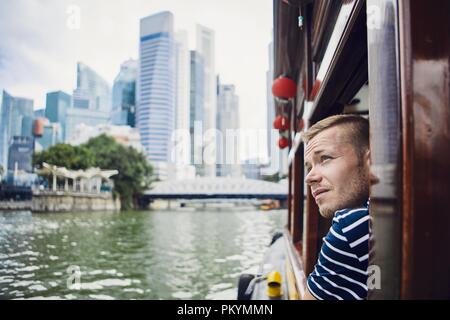 Young man exploring city and looking out from river boat in Singapore. Stock Photo