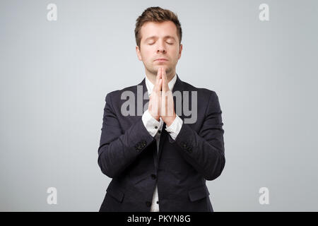 Closeup portrait of young handsome male in suit, in meditation pose, relaxing, in zen, isolated on white background Stock Photo
